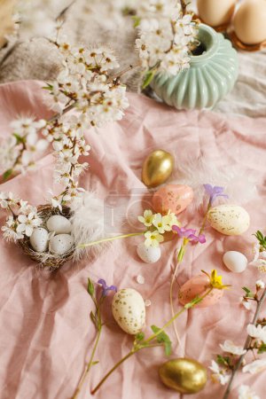 Téléchargez les photos : Happy Easter! Stylish easter eggs and blooming spring flowers on pink linen fabric. Modern eggs in nest, feathers and cherry blossoms. Rustic easter still life - en image libre de droit