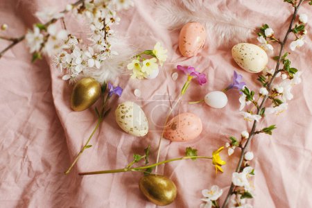 Foto de Stylish easter eggs and blooming spring flowers on pink linen fabric. Happy Easter! Modern eggs, feathers and cherry blossoms. Rustic easter still life - Imagen libre de derechos