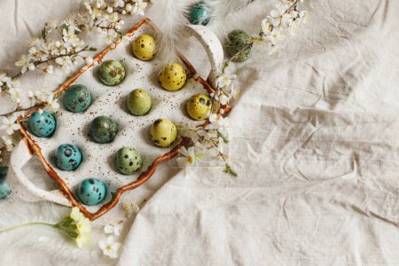 Photo for Rustic easter flat lay. Stylish easter eggs and blooming spring flowers on linen fabric. Happy Easter! Natural painted quail eggs in tray, feathers and cherry blossoms on rural table - Royalty Free Image