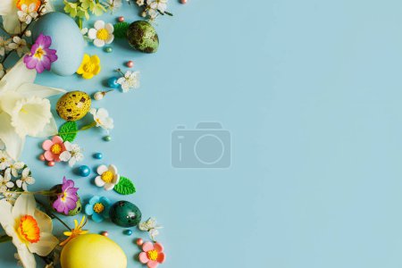 Photo for Happy Easter! Easter flat lay with stylish eggs and blooming spring flowers on blue background, space for text. Modern greeting card or banner. Natural painted colorful eggs and blossom - Royalty Free Image