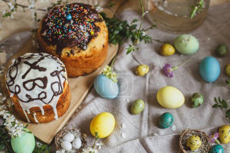 Téléchargez les photos : Homemade easter bread and natural dyed easter eggs with spring flowers on linen napkin on rustic table. Traditional Easter food. Top view. Happy Easter! - en image libre de droit