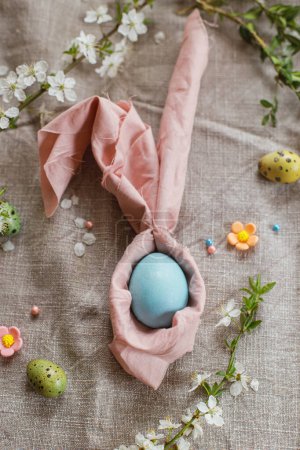 Photo for Stylish natural dyed easter egg in bunny ears napkin with spring flowers on rustic table. Happy Easter! Modern easter table setting. Rustic Easter still life - Royalty Free Image