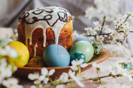 Foto de Happy Easter! Homemade easter bread and natural dyed easter eggs with spring flowers on wooden plate on rustic table. Traditional Easter food. - Imagen libre de derechos