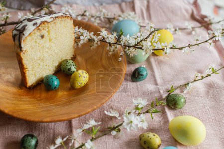 Téléchargez les photos : Homemade easter bread and natural dyed easter eggs with spring flowers on wooden plate on rustic table. Traditional Easter food. Happy Easter! Half of baked easter cake - en image libre de droit