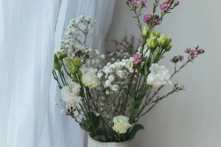 Téléchargez les photos : Stylish spring flowers, eustoma, gypsophila and chamelaucium on background of rustic wall. Floral greetings. Happy women's day and mother's day. Modern bouquet - en image libre de droit