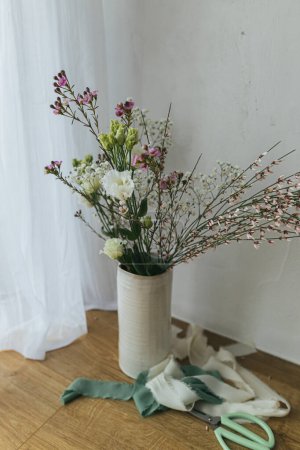 Foto de Stylish silk ribbons and modern bouquet in vase against rustic wall. Greeting card, space for text. Happy women's day and mother's day concept - Imagen libre de derechos
