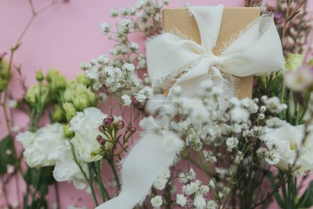 Foto de Stylish simple gift with ribbon and beautiful tender flowers on pink background flat lay. Happy womens day and mother's day concept. Floral greeting card or banner - Imagen libre de derechos