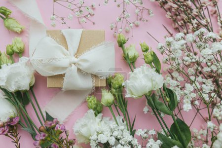 Téléchargez les photos : Élégant cadeau simple avec ruban et belles fleurs tendres sur fond rose plat laïc. Joyeuse journée des femmes et concept de fête des mères. Carte de voeux ou bannière florale - en image libre de droit