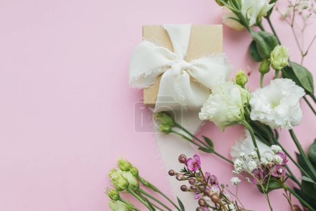 Foto de Elegante regalo simple con cinta y hermosas flores tiernas sobre fondo rosa plano con espacio para el texto. Feliz día de las mujeres y el concepto del día de la madre. Tarjeta de felicitación floral o banner - Imagen libre de derechos