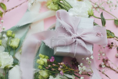 Photo for Happy womens day and mother's day concept. Stylish simple gift with ribbon and beautiful tender flowers on pink background flat lay. Floral greeting card or banner - Royalty Free Image