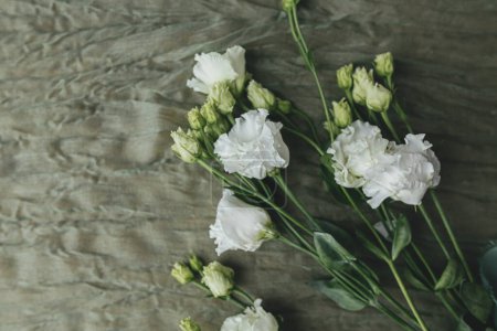 Foto de Elegantes hermosas flores blancas sobre fondo de tela verde plano laico. Bodegón floral moderno. Ramo de eustoma de primavera. Feliz día de la mujer y día de la madre. Concepto de boda - Imagen libre de derechos