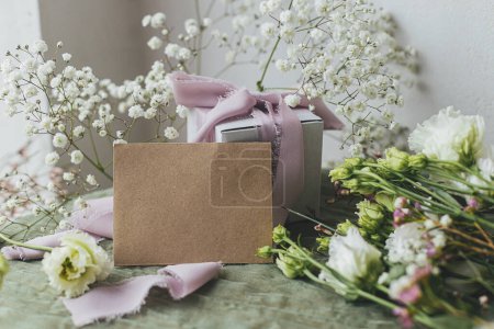 Foto de Stylish empty card, gift and beautiful flowers with ribbons on green fabric background. Happy women's day and mother's day concept. Greeting card template, space for text - Imagen libre de derechos