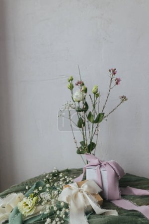 Foto de Stylish simple gift with silk ribbons and modern bouquet on green fabric against rustic wall. Happy women's day and mother's day concept. Modern spring holiday still life. Greeting card - Imagen libre de derechos