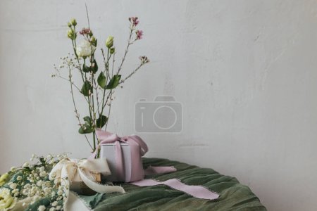 Téléchargez les photos : Happy women's day and mother's day concept. Stylish simple gift with silk ribbons and modern tender bouquet against rustic wall. Spring holiday still life. Greeting card, space for text - en image libre de droit