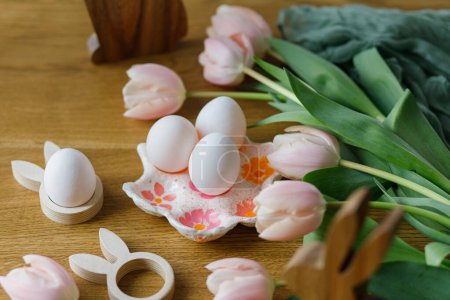 Photo for Beautiful tulips, natural eggs and bunny decoration on rustic wooden table. Happy Easter! Modern farmhouse easter decor. Stylish handmade egg holder, pink tulips and wooden bunny - Royalty Free Image