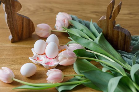 Foto de Hermosos tulipanes, huevos naturales y decoración de conejos en una mesa de madera rústica. ¡Feliz Pascua! Moderna casa de campo decoración de Pascua. Elegante titular de huevo hecho a mano, tulipanes rosados y conejito de madera - Imagen libre de derechos