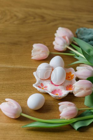 Téléchargez les photos : Joyeux Pâques ! Belles tulipes et œufs sur table en bois. Ferme moderne décor de Pâques. Porte-œufs élégant fait à la main avec des œufs naturels et des tulipes roses - en image libre de droit