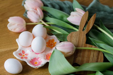 Photo for Happy Easter! Beautiful tulips, eggs and bunny decoration on wooden table. Modern farmhouse easter decor. Stylish handmade egg holder, natural eggs, pink tulips and rustic bunny - Royalty Free Image