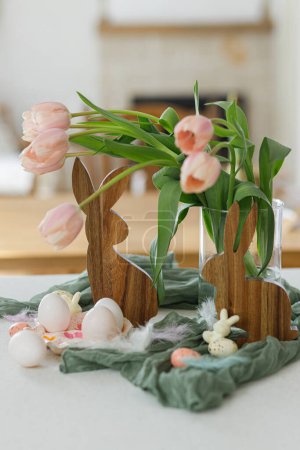 Foto de Hermosos tulipanes, huevos naturales y decoración de conejos en la mesa moderna. ¡Feliz Pascua! Elegante casa de campo decoración de Pascua. Porta huevos hecho a mano, tulipanes rosados y conejito de madera - Imagen libre de derechos