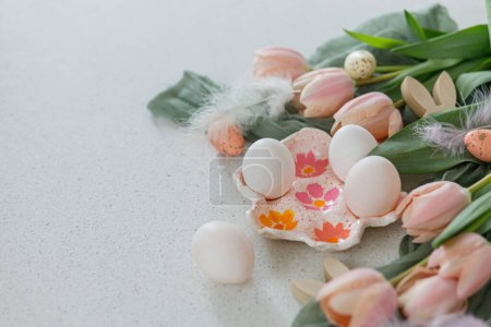Téléchargez les photos : Joyeux Pâques ! Belles tulipes, œufs naturels et décoration de lapin sur table moderne. Pâques élégant nature morte avec espace de copie. Porte-œufs fait main, tulipes roses et oreilles de lapin en bois - en image libre de droit