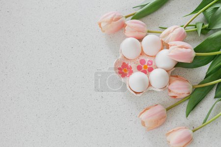 Téléchargez les photos : Joyeux Pâques ! Belles tulipes et œufs naturels sur table moderne. Élégant Pâques plat couché avec espace de copie. Porte-œufs à la main avec tulipes roses - en image libre de droit