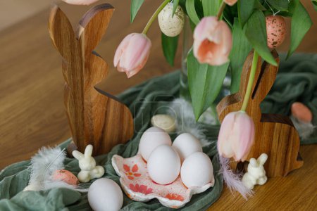 Foto de Hermosos tulipanes, huevos y decoración de conejos en mesa de madera. Moderna casa de campo decoración de Pascua. ¡Feliz Pascua! Elegante porta huevos hecho a mano, huevos naturales, ramo de tulipanes rosados y conejos rústicos - Imagen libre de derechos