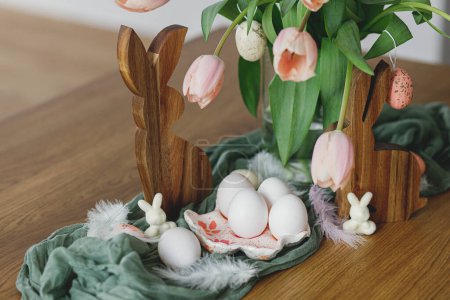 Téléchargez les photos : Belles tulipes, œufs et décoration de lapin sur table en bois. Ferme moderne décor de Pâques. Joyeux Pâques ! Porte-œufs artisanal élégant, œufs naturels, bouquet de tulipes roses et lapins rustiques - en image libre de droit