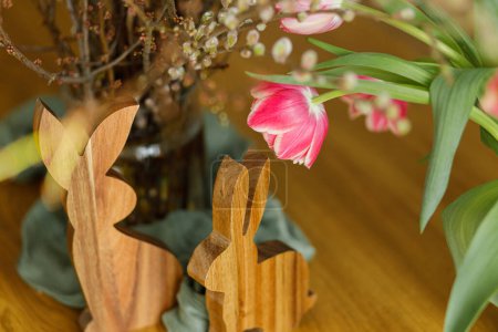 Photo for Stylish bunny and tulips on wooden table close up. Happy Easter! Tulips and willow branches bouquet with easter decor in dining room in farmhouse. Rustic arrangement - Royalty Free Image