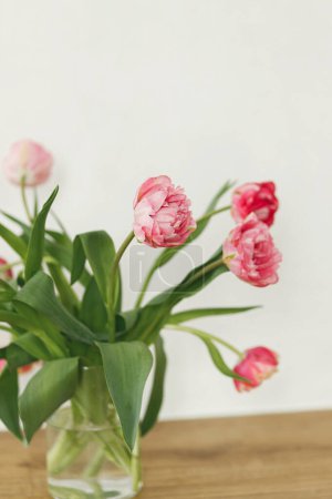 Photo for Stylish beautiful tulips bouquet in vase on wooden table in rustic room. Floral festive arrangement in farmhouse. Spring flowers composition. Happy mothers day and womens - Royalty Free Image