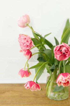 Téléchargez les photos : Élégant bouquet de tulipes roses dans un vase sur table en bois dans une pièce rustique. Arrangement floral dans la ferme. Composition fleurs de printemps, espace de copie. Joyeuse fête des mères et des femmes - en image libre de droit