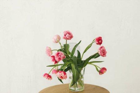 Foto de Elegante hermoso ramo de tulipanes rosados en jarrón sobre mesa de madera en habitación rústica. Arreglo floral en granja. Composición de flores de primavera, espacio de copia. Feliz día de las madres y las mujeres - Imagen libre de derechos
