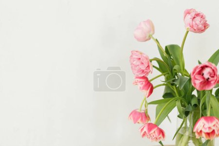 Foto de Elegante hermoso ramo de tulipanes rosados sobre fondo rústico de pared blanca. Arreglo floral en granja. Composición de flores de primavera, espacio de copia. Feliz día de las madres y las mujeres - Imagen libre de derechos