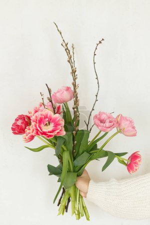 Photo for Stylish pink tulips with willow branches in hand on white wall background. Woman holding beautiful spring bouquet. Happy mothers day and womens day. Happy Easter - Royalty Free Image