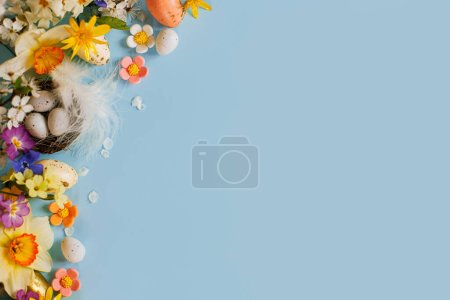 Téléchargez les photos : Des œufs de Pâques élégants dans le nid, des fleurs colorées et des fleurs de cerisier à plat reposent sur un fond bleu avec un espace de copie. Joyeux Pâques ! Modèle de carte de vœux. Bannière de vacances moderne. Composition festive - en image libre de droit