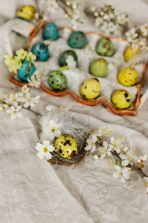 Photo for Rustic easter still life. Stylish easter eggs and blooming spring flowers on linen fabric. Happy Easter! Natural painted quail eggs in tray, feathers and cherry blossoms on rural table - Royalty Free Image
