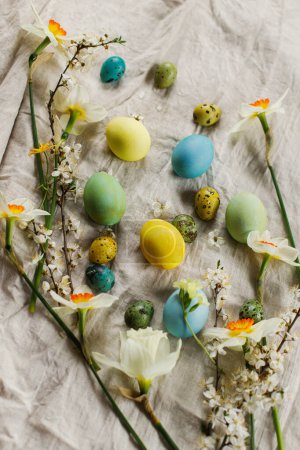 Foto de Pascuas rústicas. Elegantes huevos de Pascua y flores florecientes de primavera en la mesa rústica. ¡Feliz Pascua! Huevos naturales pintados y narcisos florecen sobre tela de lino - Imagen libre de derechos