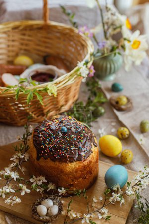Homemade easter bread, natural dyed easter eggs, ham, beets, butter in basket on rustic table with spring blossoms and linen napkin. Top view. Traditional Easter food