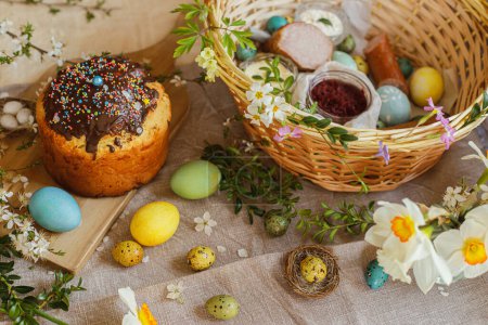 Foto de Homemade easter bread, natural dyed easter eggs, ham, beets, butter in basket on rustic table with spring blossoms and linen napkin. Top view. Traditional Easter food - Imagen libre de derechos