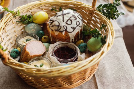 Photo for Traditional Easter food in basket. Homemade easter bread, natural dyed easter eggs, ham, beets, butter, cheese on rustic table with spring blossoms. Top view - Royalty Free Image