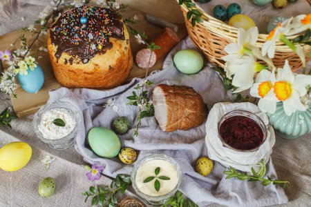 Photo for Traditional Easter food. Homemade easter bread, natural dyed easter eggs, ham, beets, butter, cheese on linen napkin on rustic table with spring flowers. Top view. - Royalty Free Image