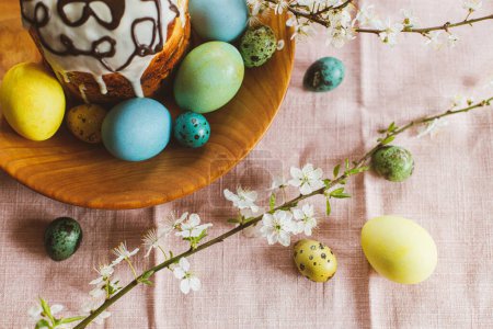 Téléchargez les photos : Homemade easter bread and natural dyed easter eggs with spring flowers on wooden plate on rustic table. Top view. Happy Easter! Traditional Easter food. - en image libre de droit