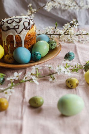 Téléchargez les photos : Joyeux Pâques ! Pain de Pâques fait maison et œufs de Pâques teints naturellement avec des fleurs de printemps sur une assiette en bois sur une table rustique. Nourriture traditionnelle de Pâques. - en image libre de droit