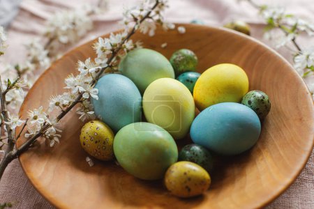Foto de ¡Feliz Pascua! Elegantes huevos naturales de Pascua teñidos en un plato de madera con flores de primavera en una mesa rústica.Comida tradicional de Pascua. Pascua rústica naturaleza muerta - Imagen libre de derechos