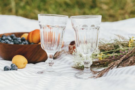 Foto de Summer picnic and vacation concept. Tasty fruits and berries, wineglasses and bouquet of wildflowers on blanket. Blueberries, peaches and apricots - Imagen libre de derechos