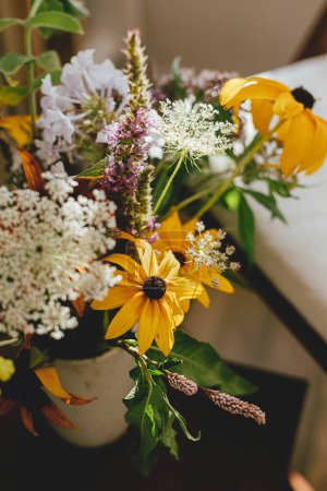 Téléchargez les photos : Bouquet de fleurs sauvages sur fond de chaise en bois avec oreiller blanc dans une pièce rustique ensoleillée. L'été à la campagne. Accueil décor écologique simple, belles fleurs jaunes - en image libre de droit