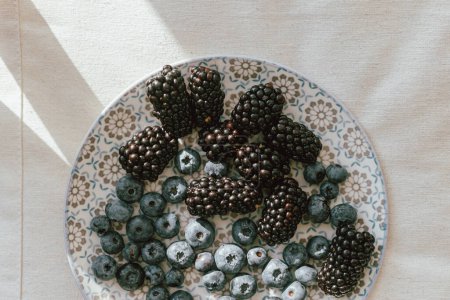 Téléchargez les photos : Fresh blueberries and blackberries in sunlight on ceramic plate flat lay. Healthy food aesthetics. Summer berries in light on soft linen background. Summer in countryside, moody banner - en image libre de droit