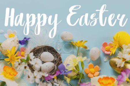 Photo for Happy Easter greeting card. Happy Easter text on stylish Easter eggs in nest, colorful flowers and cherry blossoms flat lay on blue background. Modern Greeting card. Handwritten sign - Royalty Free Image