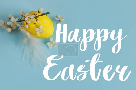 Téléchargez les photos : Joyeux texte de Pâques signe sur oeuf jaune de Pâques et fleurir sur fond bleu plat pondre. Carte de vœux de Pâques moderne. Lettrage manuscrit - en image libre de droit