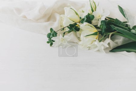 Foto de Feliz Día de las Madres. Hermosos tulipanes blancos y narcisos sobre tela suave sobre mesa de madera rústica con espacio para texto. Elegante ramo de primavera del jardín. Día de las mujeres - Imagen libre de derechos