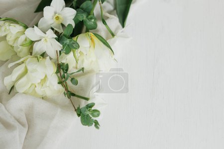 Foto de Hermosos tulipanes blancos y narcisos sobre tela suave sobre mesa de madera rústica plana con espacio para el texto. Feliz Día de las Madres. Elegante ramo de primavera del jardín. Día de las mujeres - Imagen libre de derechos